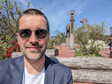 Picture of Philipp Beckerle sitting in the sun with sunglases on, smiling into the camera