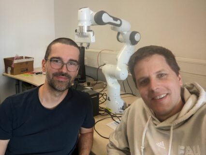 auf der linken Seite sieht man Philipp Beckerle, auf der rechten Seite Bernhard Egger, im Hintergrund ist ein weißer Roboterarm